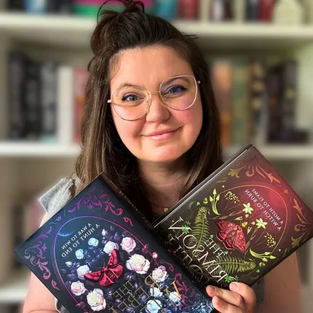 Mathilde, fondatrice de Neloory, tenant deux romans de fantasy devant sa bibliothèque.